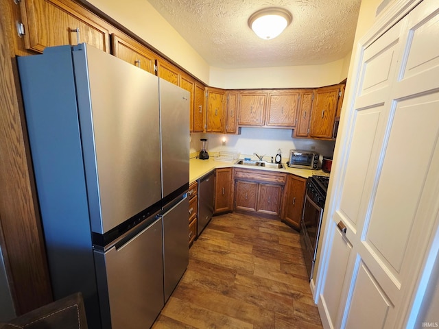 kitchen featuring dark wood-style floors, a sink, a textured ceiling, brown cabinets, and appliances with stainless steel finishes