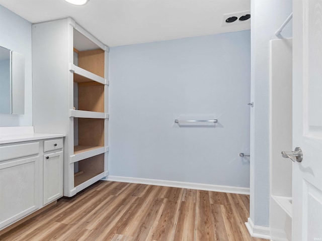 bathroom featuring a bath, baseboards, vanity, and wood finished floors