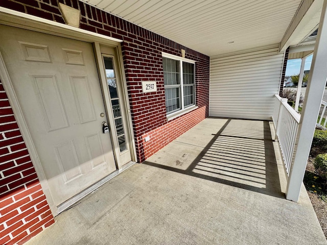 view of exterior entry featuring brick siding and covered porch