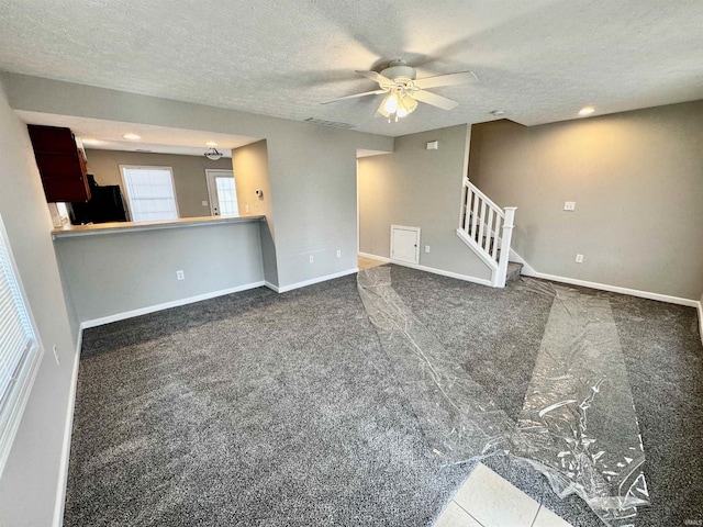 unfurnished living room with stairway, ceiling fan, carpet floors, and a textured ceiling
