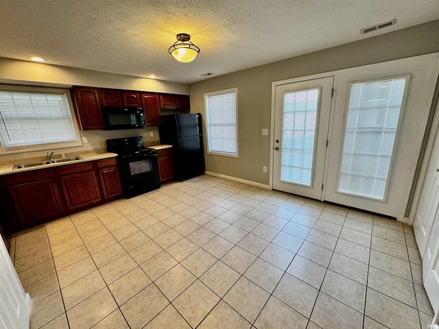 kitchen with a textured ceiling, a sink, black appliances, light countertops, and visible vents