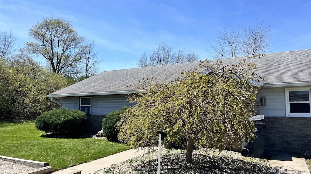 view of side of property with brick siding, roof with shingles, and a lawn