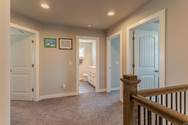 hall with an upstairs landing, carpet floors, baseboards, visible vents, and recessed lighting