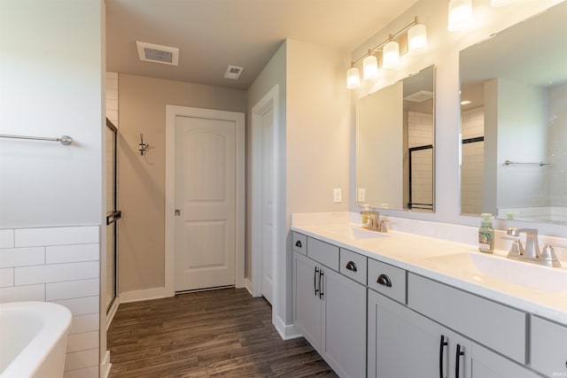full bath with wood finished floors, visible vents, a tub, and a sink