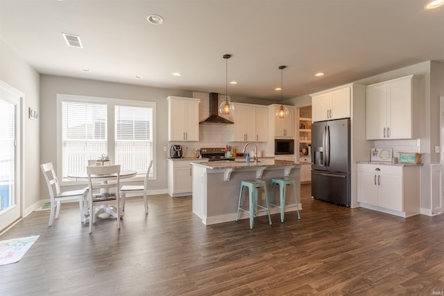 kitchen with wall chimney range hood, a sink, electric range, stainless steel refrigerator with ice dispenser, and visible vents