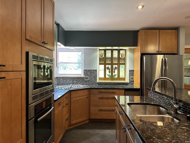 6065 Gladden Dr, Indianapolis, IN 46220 - kitchen featuring stainless steel appliances, a sink, dark stone countertops, backsplash, and brown cabinets