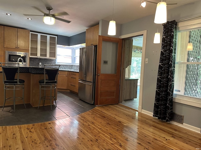 6065 Gladden Dr, Indianapolis, IN 46220 - kitchen featuring a ceiling fan, glass insert cabinets, a breakfast bar area, stainless steel appliances, and wood-type flooring