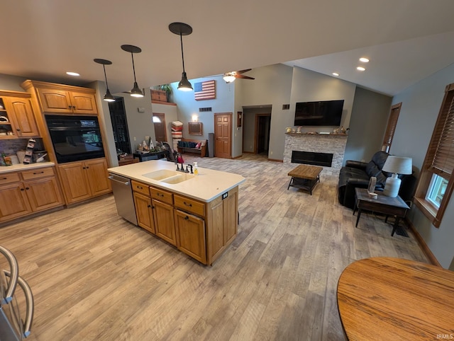 kitchen with a sink, light wood-style floors, dishwasher, light countertops, and black oven
