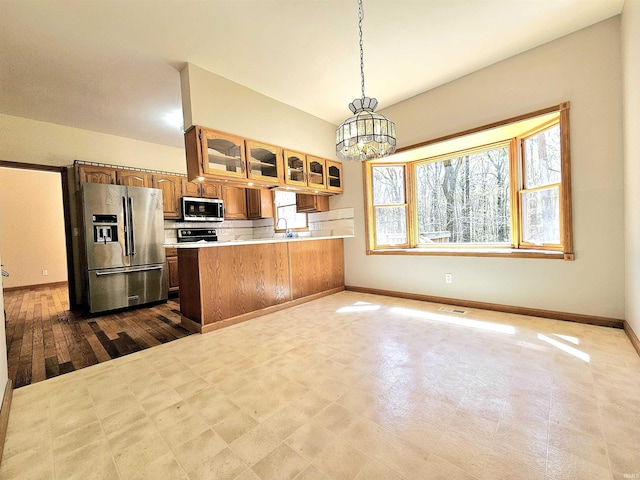 kitchen with light countertops, backsplash, baseboards, glass insert cabinets, and appliances with stainless steel finishes