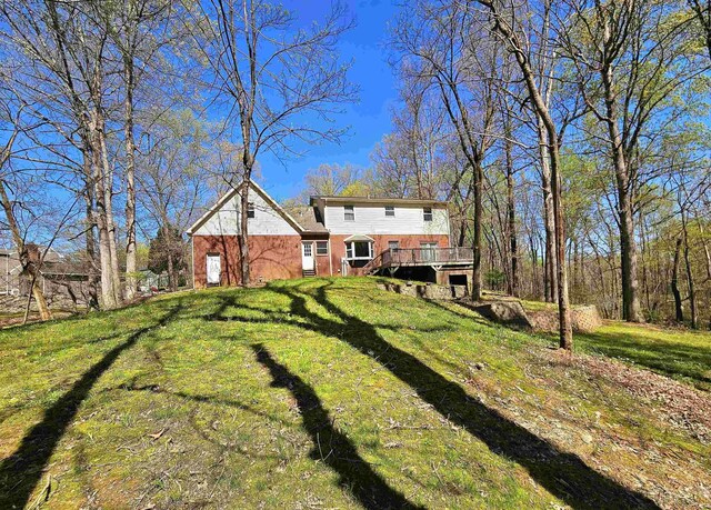 back of property featuring a wooden deck, a lawn, and brick siding