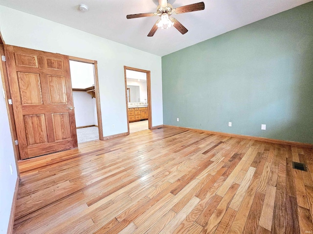 unfurnished bedroom with ensuite bathroom, a spacious closet, light wood-type flooring, baseboards, and visible vents