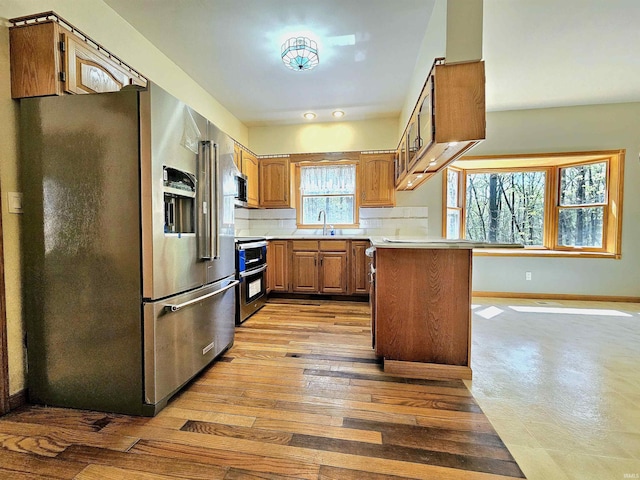 kitchen with stainless steel appliances, a sink, baseboards, brown cabinetry, and light countertops