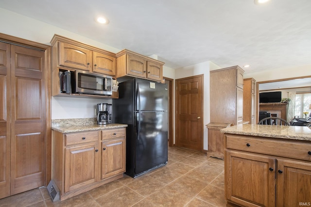 kitchen featuring brown cabinets, recessed lighting, light stone counters, stainless steel microwave, and freestanding refrigerator
