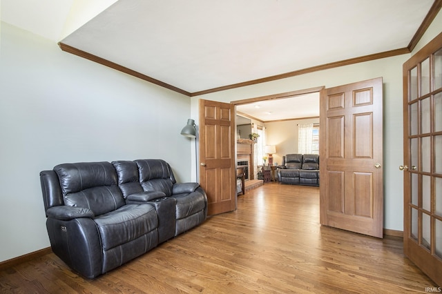 living area featuring light wood-type flooring, a fireplace with raised hearth, baseboards, and ornamental molding