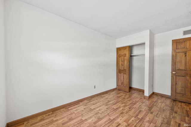 unfurnished bedroom with a closet, light wood-style flooring, baseboards, lofted ceiling, and visible vents