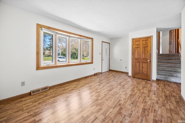 unfurnished living room with baseboards, light wood-style flooring, visible vents, and stairs