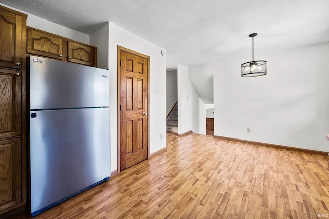 kitchen with baseboards, freestanding refrigerator, light wood-style floors, and hanging light fixtures