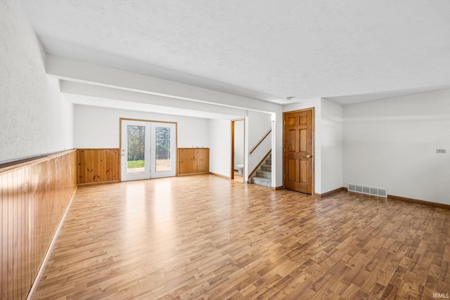 unfurnished living room with wooden walls, wood finished floors, a wainscoted wall, and stairway