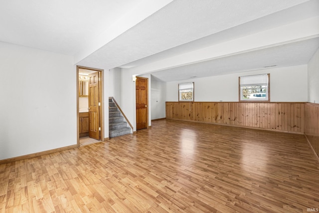 below grade area with wainscoting, baseboards, light wood-style floors, wood walls, and stairs