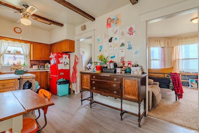kitchen featuring beamed ceiling, brown cabinetry, light wood-style flooring, and a ceiling fan
