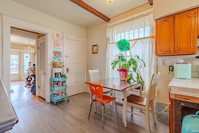 dining room with a notable chandelier, beamed ceiling, and light wood-style flooring