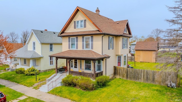 victorian home with covered porch, fence, an outbuilding, a front yard, and a storage unit