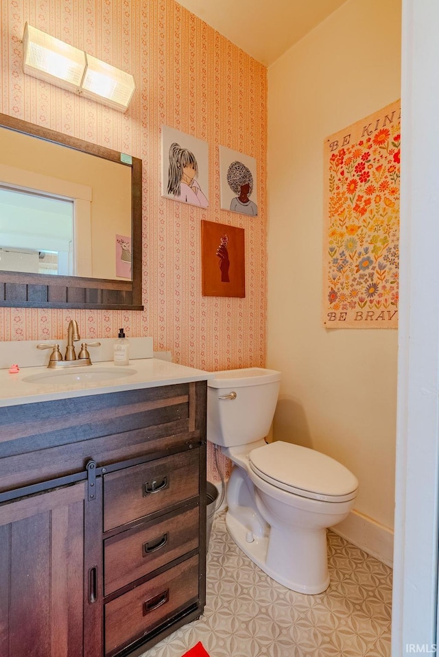 half bathroom with toilet, baseboards, wallpapered walls, tile patterned flooring, and vanity