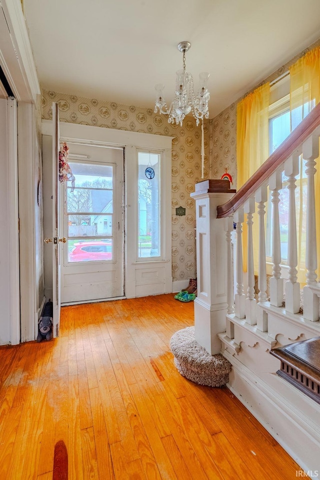 foyer with wallpapered walls, light wood-type flooring, stairway, and an inviting chandelier