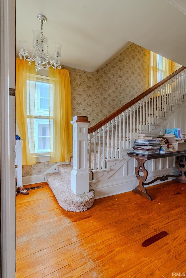 stairway with a notable chandelier, wood finished floors, and wallpapered walls