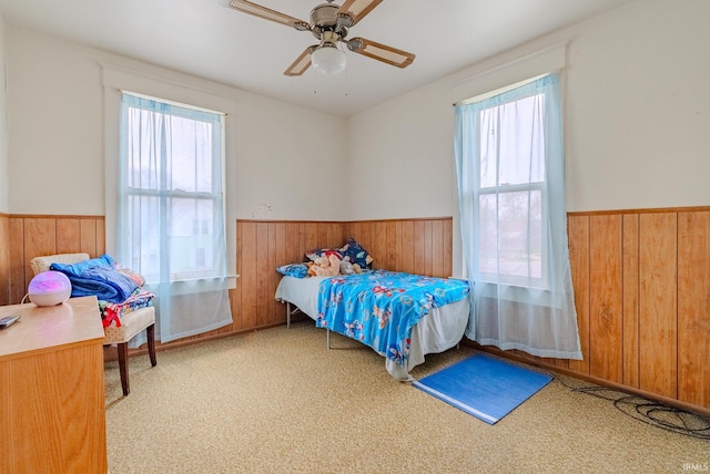 bedroom with wainscoting, wood walls, and multiple windows
