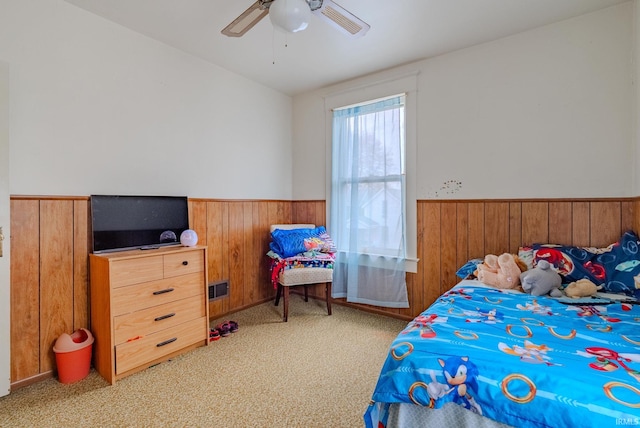 bedroom featuring wainscoting, ceiling fan, carpet flooring, and wooden walls