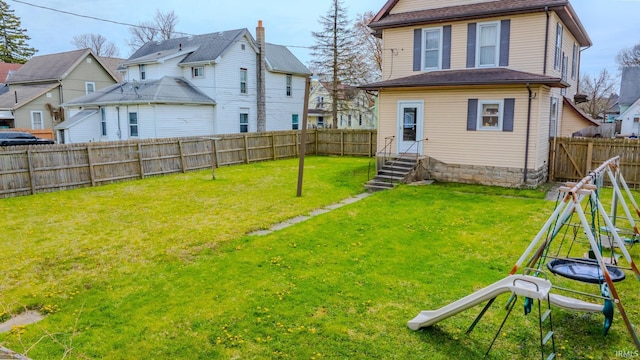 rear view of house with entry steps, a lawn, and a fenced backyard