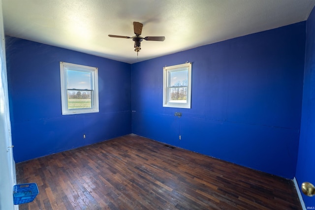empty room with a ceiling fan, dark wood-type flooring, visible vents, and plenty of natural light