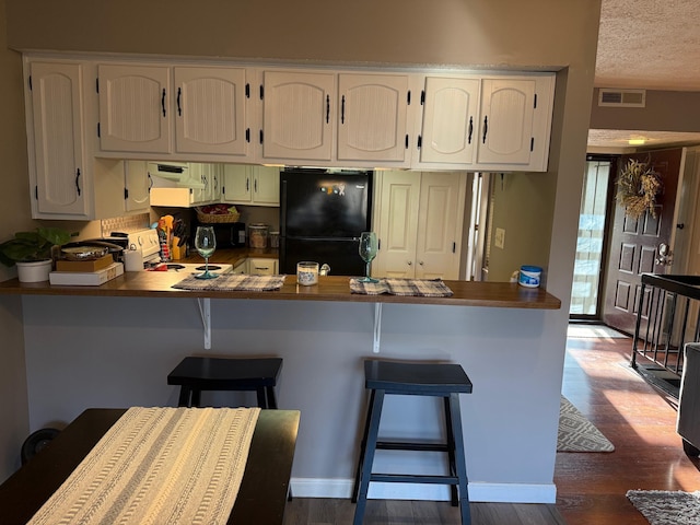 kitchen featuring exhaust hood, dark wood finished floors, a peninsula, and freestanding refrigerator