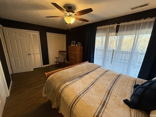 bedroom featuring wood finished floors, visible vents, a textured ceiling, and multiple closets
