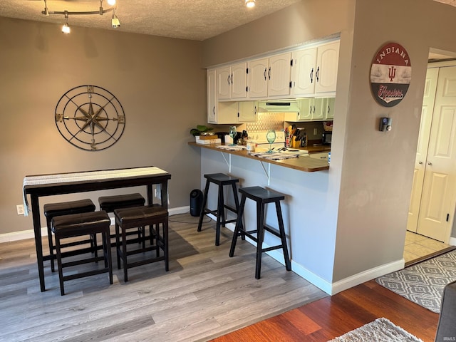 kitchen featuring a kitchen breakfast bar, a textured ceiling, light wood-type flooring, white cabinetry, and under cabinet range hood