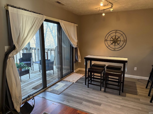 dining area with wood finished floors, a textured ceiling, baseboards, and visible vents