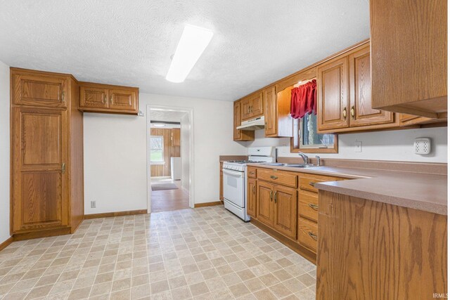 8763 E Backwater Rd, North Webster, IN 46555 - kitchen featuring brown cabinetry, under cabinet range hood, white range with gas cooktop, and a sink