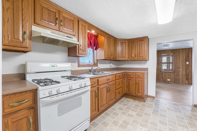 8763 E Backwater Rd, North Webster, IN 46555 - kitchen with white gas stove, under cabinet range hood, a sink, and brown cabinets