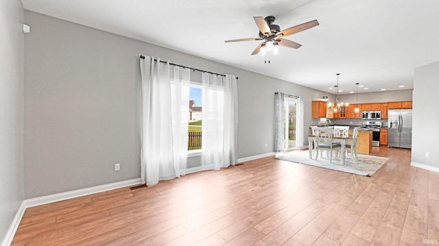 unfurnished living room featuring baseboards, light wood-style floors, visible vents, and ceiling fan with notable chandelier