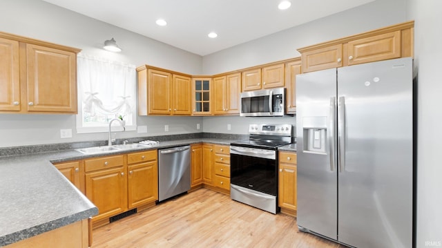 kitchen with stainless steel appliances, a sink, light wood-style floors, and dark countertops