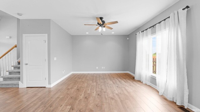 spare room with stairway, a ceiling fan, light wood-style flooring, baseboards, and visible vents