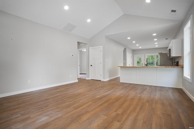 unfurnished living room with baseboards, visible vents, wood finished floors, and high vaulted ceiling