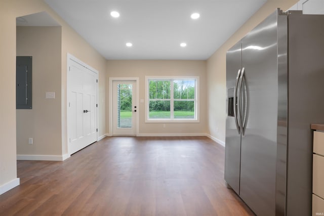 interior space featuring electric panel, stainless steel refrigerator with ice dispenser, wood finished floors, baseboards, and recessed lighting
