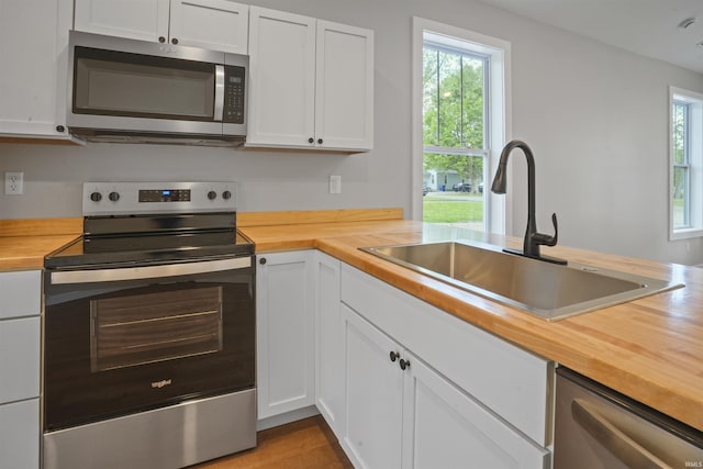 kitchen with a sink, butcher block counters, white cabinets, and stainless steel appliances