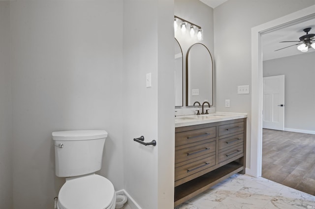 bathroom featuring vanity, toilet, marble finish floor, a ceiling fan, and baseboards