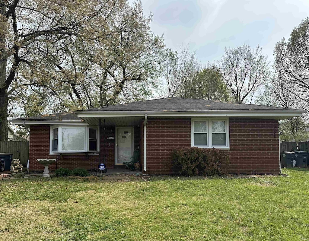 ranch-style home with fence, a shingled roof, brick siding, and a front yard