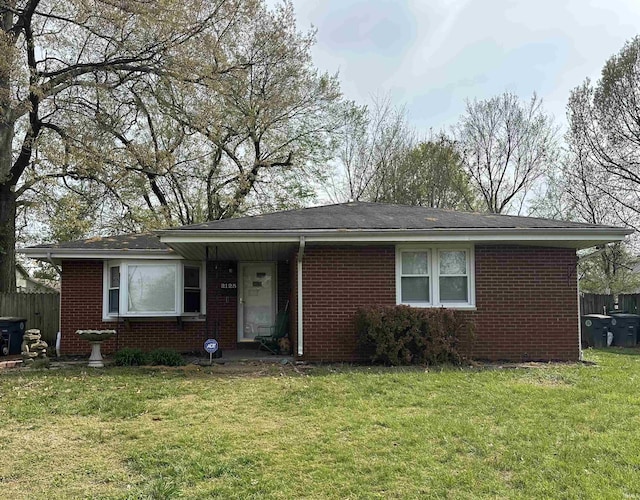 ranch-style home with fence, a shingled roof, brick siding, and a front yard