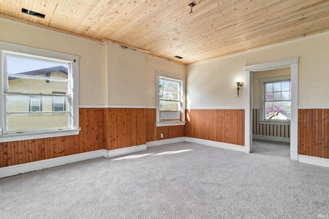 carpeted spare room featuring wainscoting, wooden ceiling, and wood walls