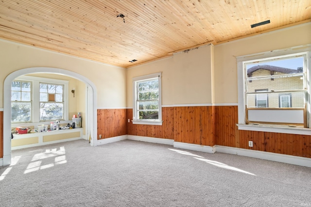 spare room featuring wainscoting, wooden walls, arched walkways, wooden ceiling, and carpet flooring